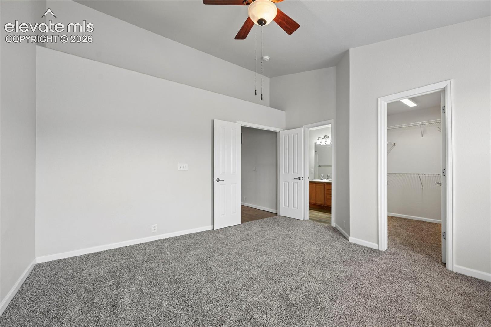 Spacious room featuring vaulted ceilings, ceiling fan with light fixture, light gray walls, and plush gray carpeting