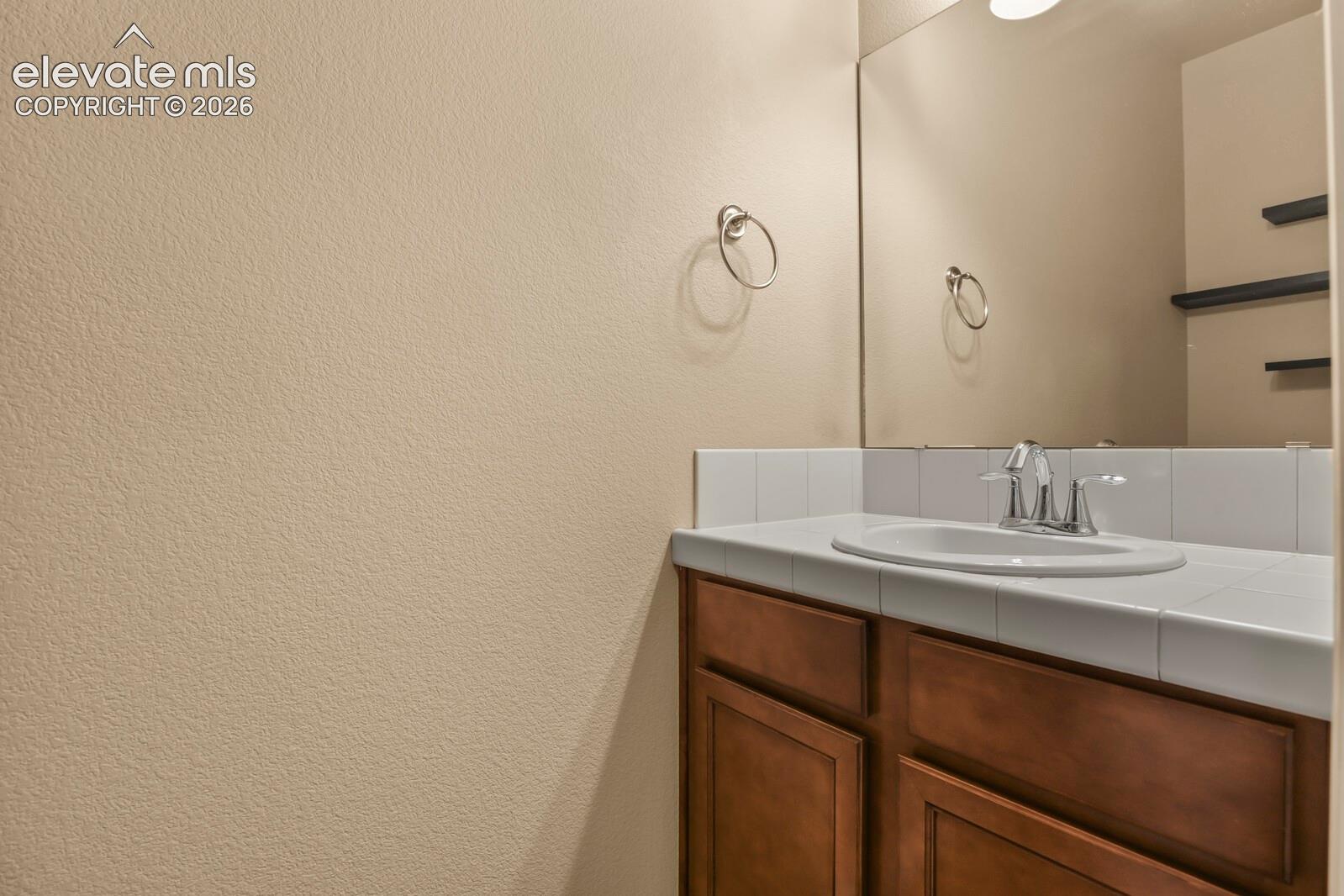 Wood-finish vanity with a drop-in sink, chrome faucet, and white tiled countertop