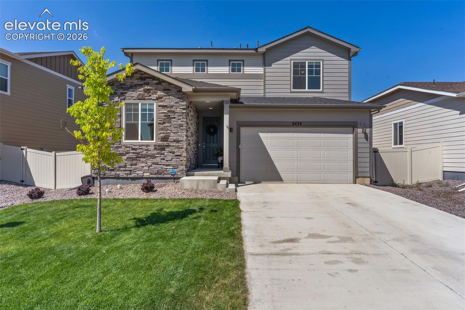 Two-story residence featuring a stone and siding facade, an attached two-car garage, an established lawn, and a concrete driveway