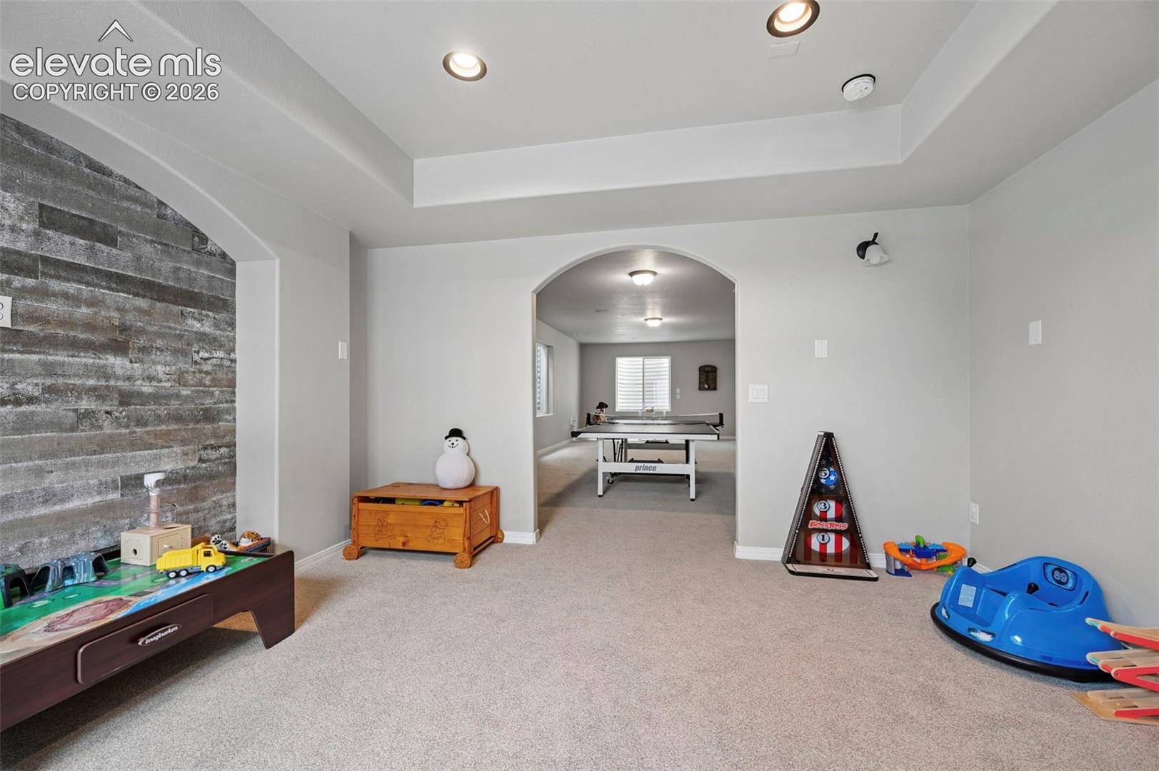 Interior space featuring a recessed tray ceiling, wood-plank accent wall, and arched passage with recessed lighting