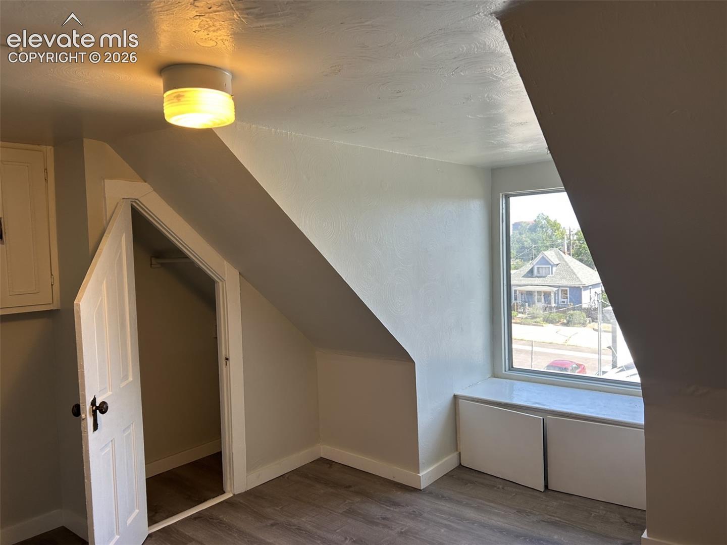 Sloped ceilings, window with integrated storage, wood-finish flooring, and a built-in closet
