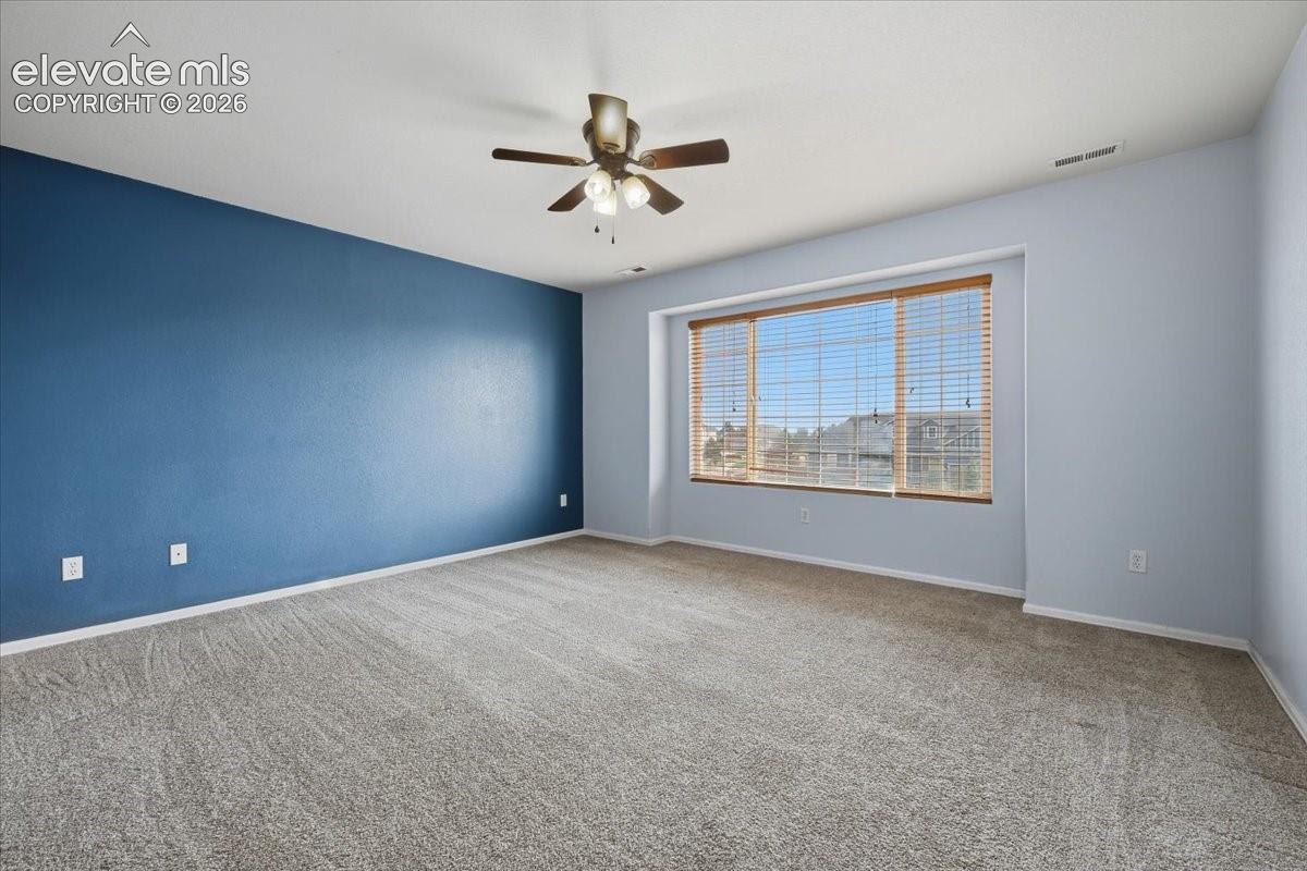 Spacious room featuring carpeting, a prominent accent wall, a multi-pane window with blinds, and a ceiling fan with integrated lighting