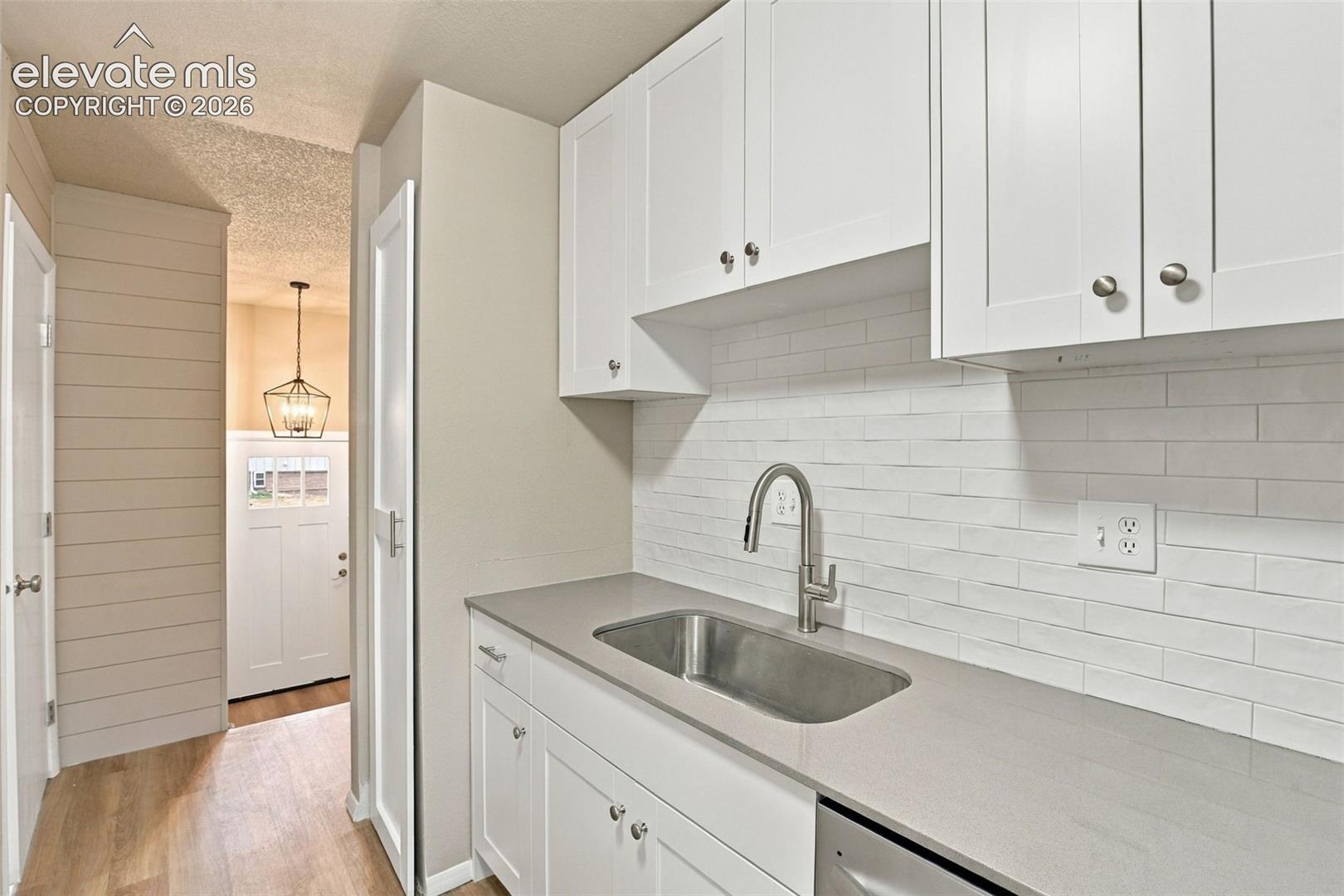 White Shaker-style cabinetry, solid-surface countertops, horizontal plank wall detailing, stainless steel undermount sink with arched pull-down faucet, and white subway tile backsplash