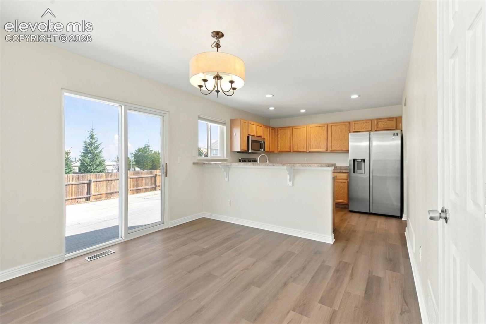 Kitchen featuring a breakfast bar with stone-finish countertops, wood-finish flooring, stainless steel side-by-side refrigerator, recessed lighting, and a drum-style chandelier
