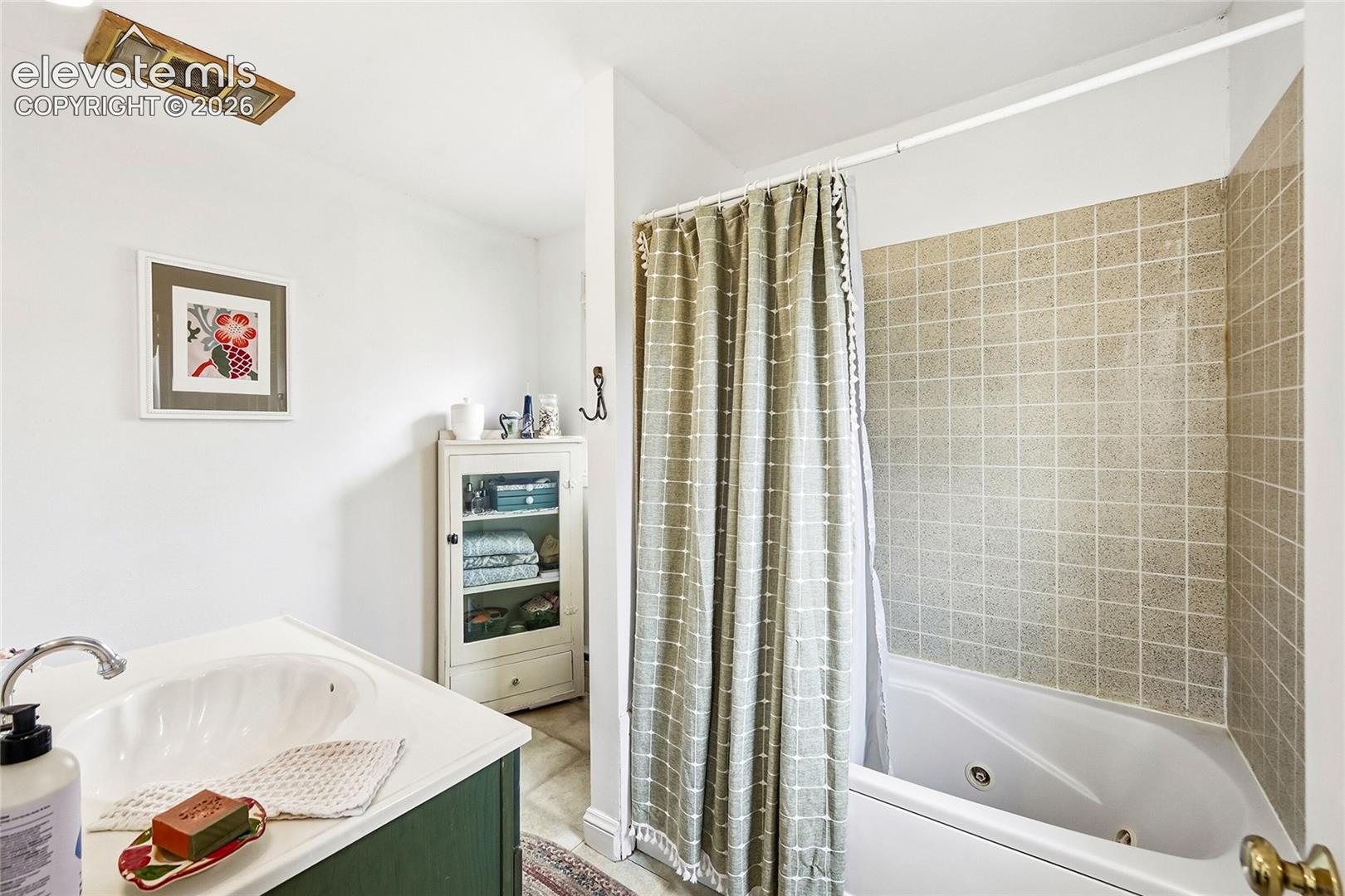 Bathroom featuring a soaking tub, square-tiled wall surround, white vanity with an integrated basin, and built-in glass-front cabinetry