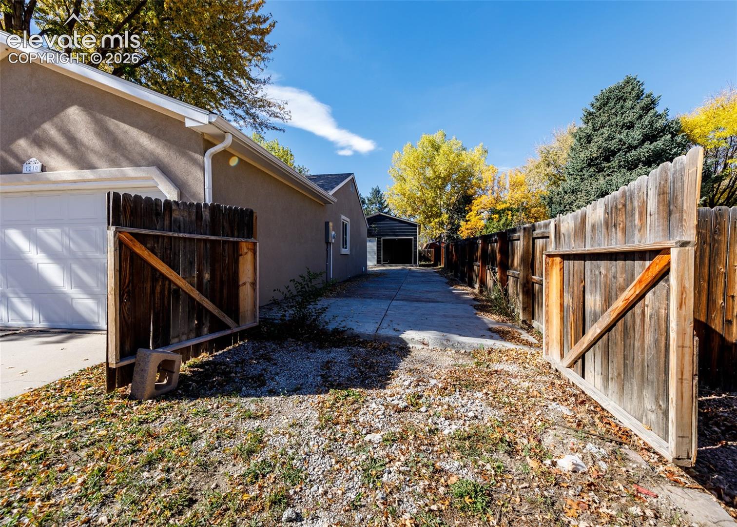 Stucco exterior featuring a paved driveway, detached garage, and enclosed wooden fencing