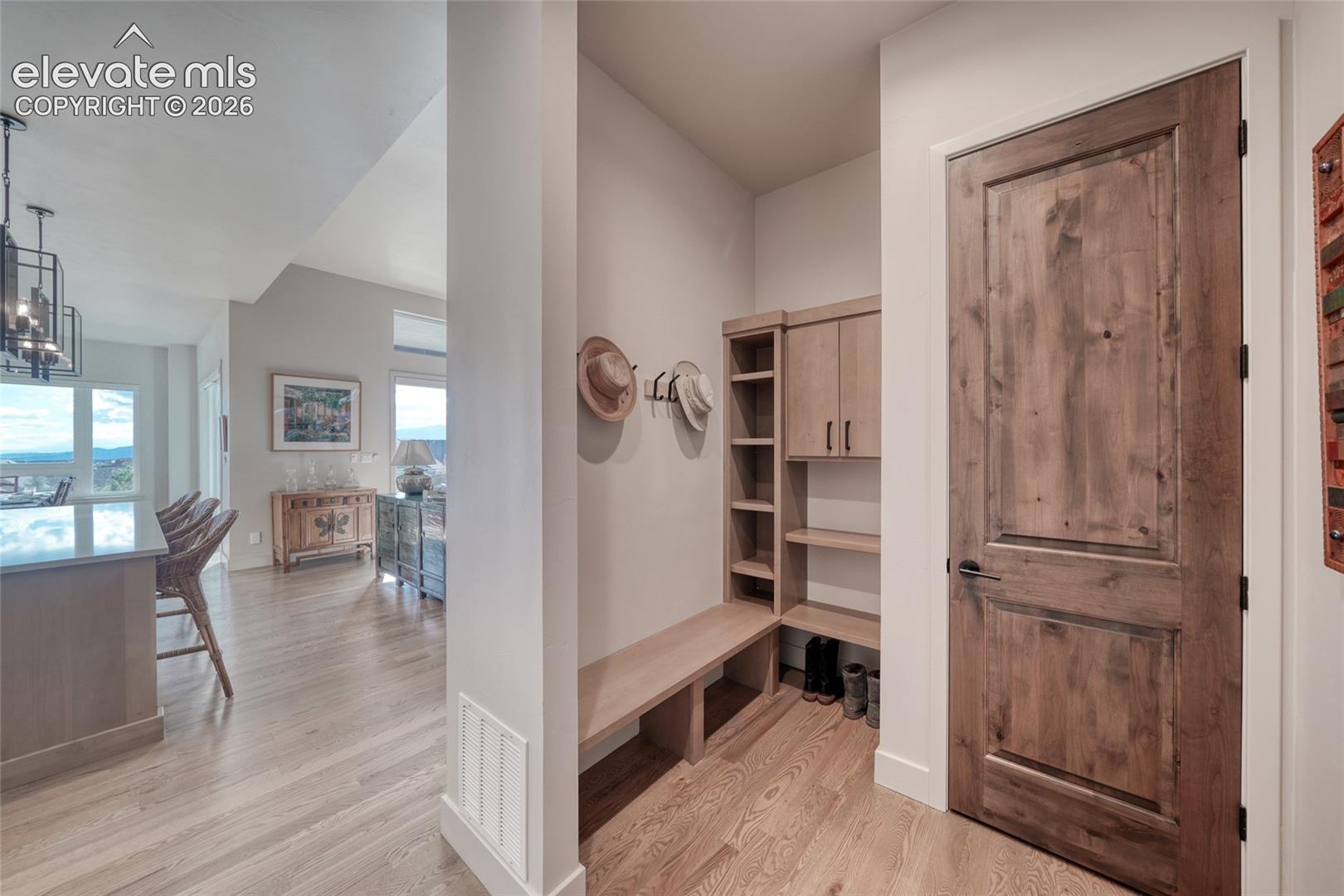 Built-in mudroom cabinetry with shelving and bench seating, wood-finish interior door, and wood-finish flooring