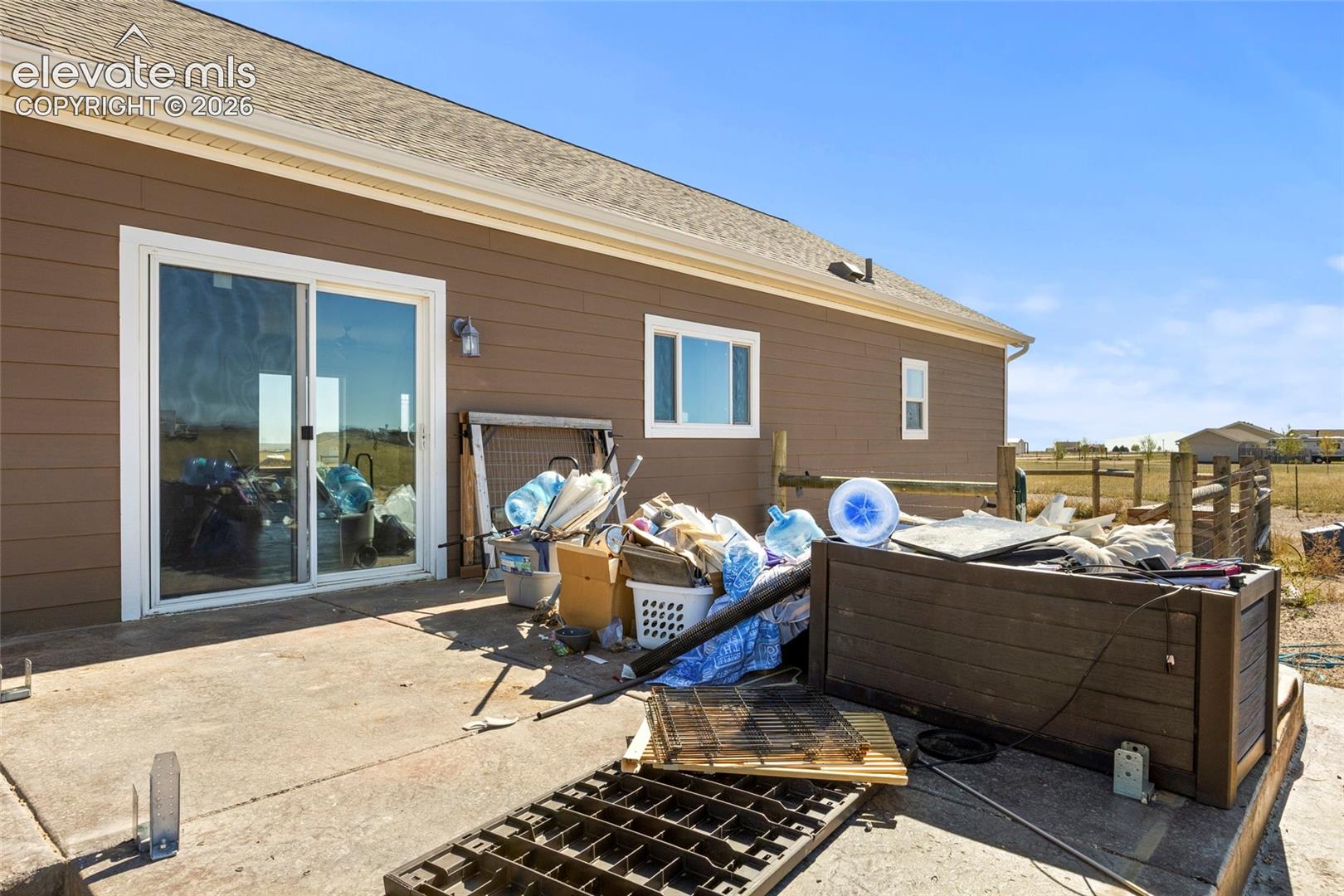 Horizontal siding exterior featuring a concrete patio, sliding glass door, and a split-rail perimeter fence