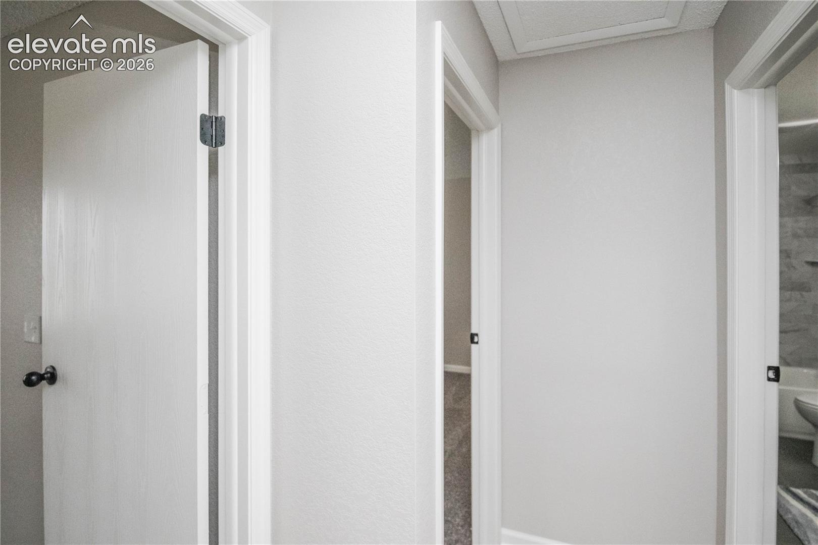 Interior corridor featuring neutral painted walls, white door casings, and solid-core interior doors with matte black hardware