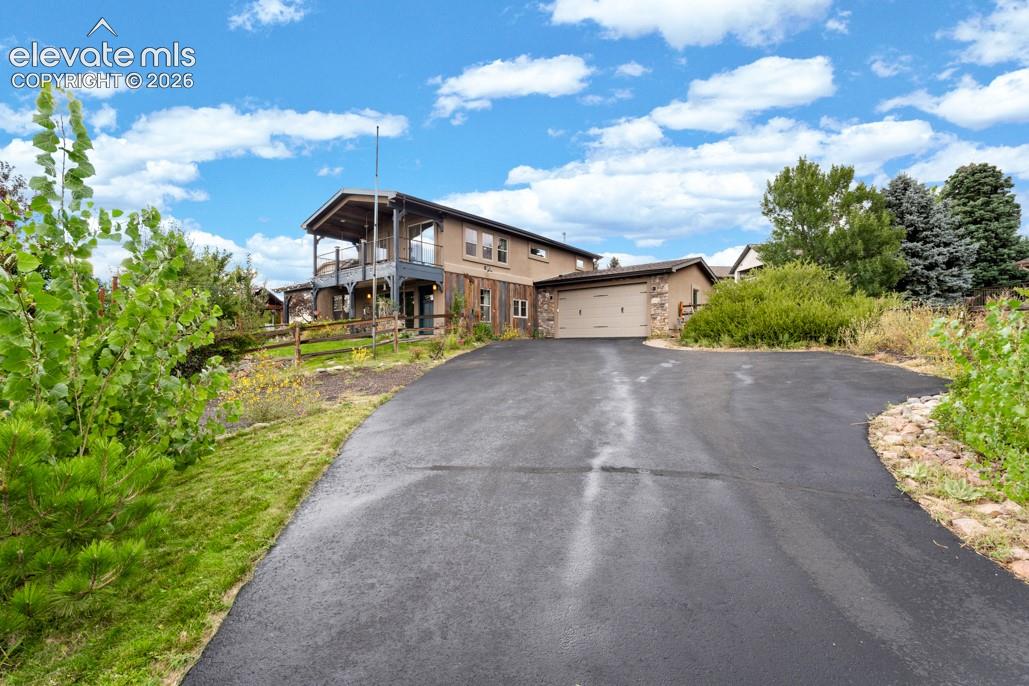 Paved driveway leading to a two-story residence featuring a covered balcony, an attached garage, and stone facade accents