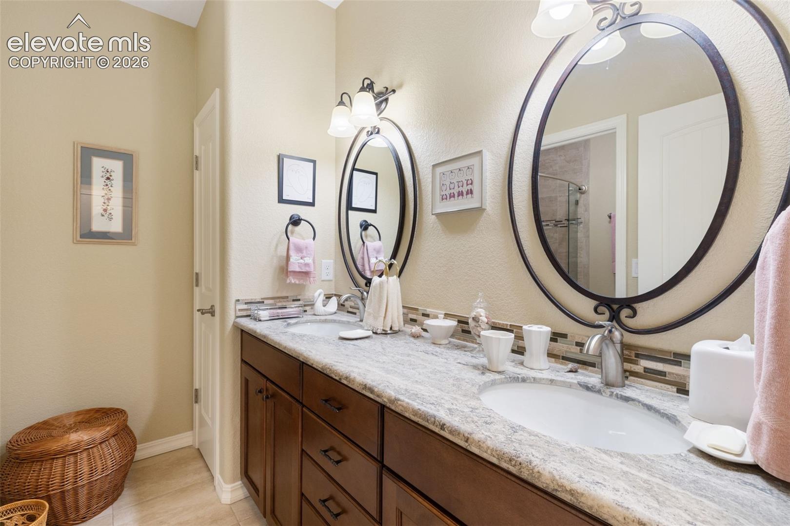 Dual vanity featuring a light-toned granite countertop, undermount sinks, birch cabinetry, and decorative framed mirrors