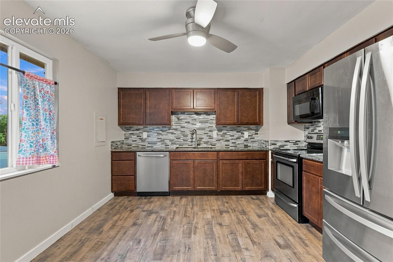 Kitchen featuring wood-finish flooring, dark wood cabinetry, stainless steel appliances, granite counter-tops and a mosaic tile backsplash