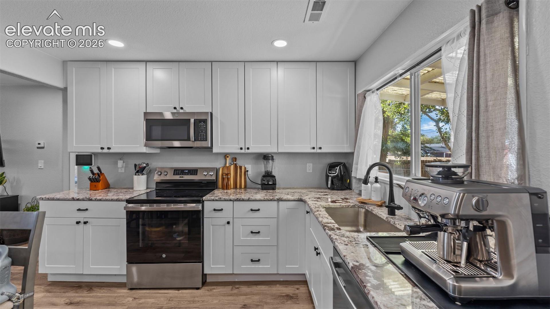 Kitchen featuring white cabinetry, stone-surface countertops, stainless steel appliances, a stainless steel undermount sink, and recessed lighting