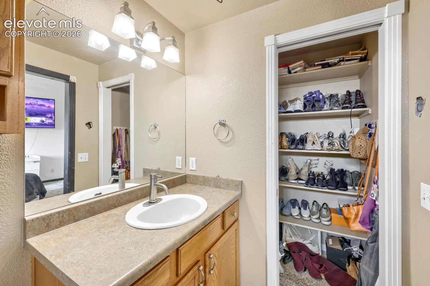 Vanity with an integrated sink and brushed nickel faucet, large wall mirror, and built-in closet shelving