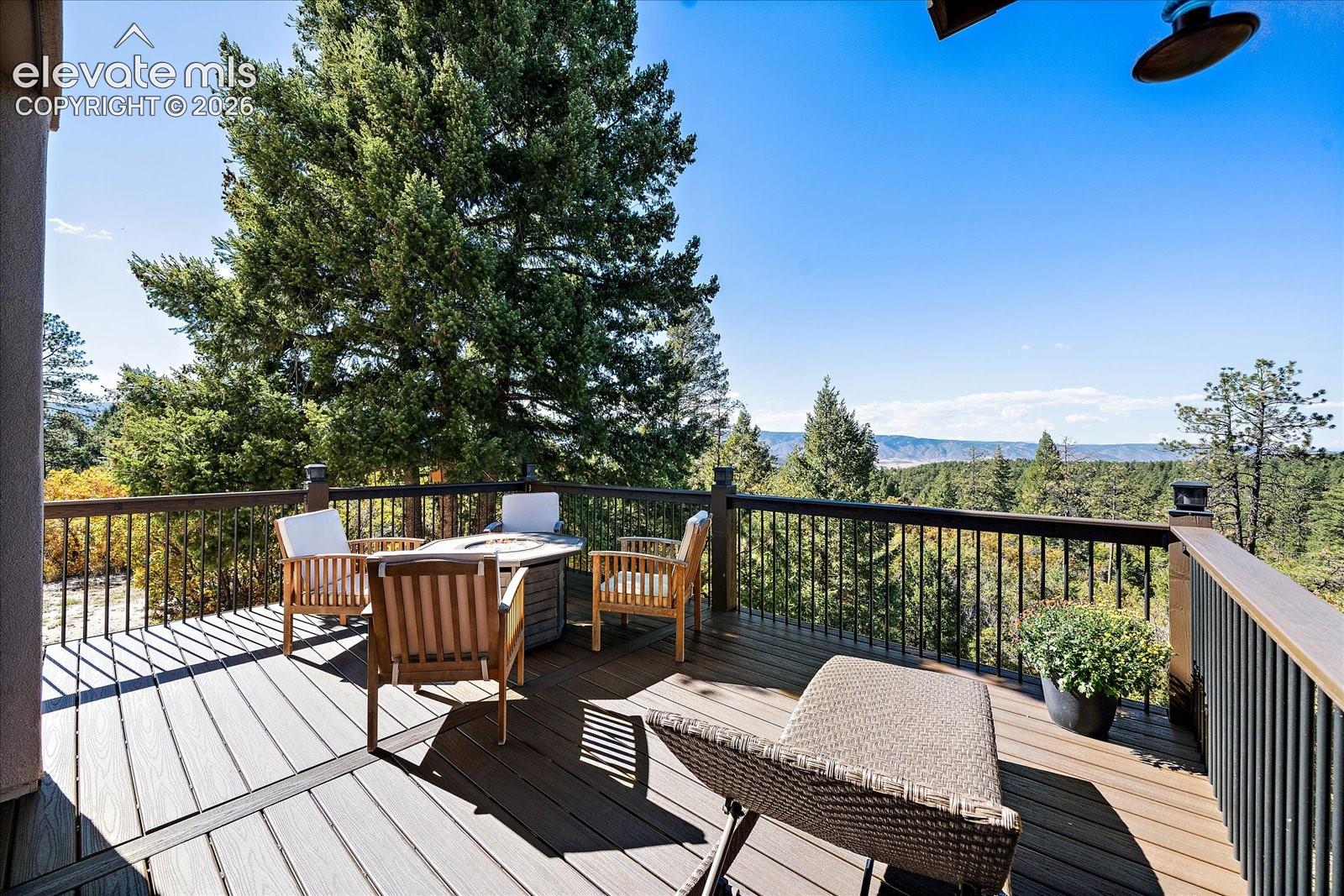 Elevated composite deck with metal railings, featuring mature evergreen trees and distant mountain scenery