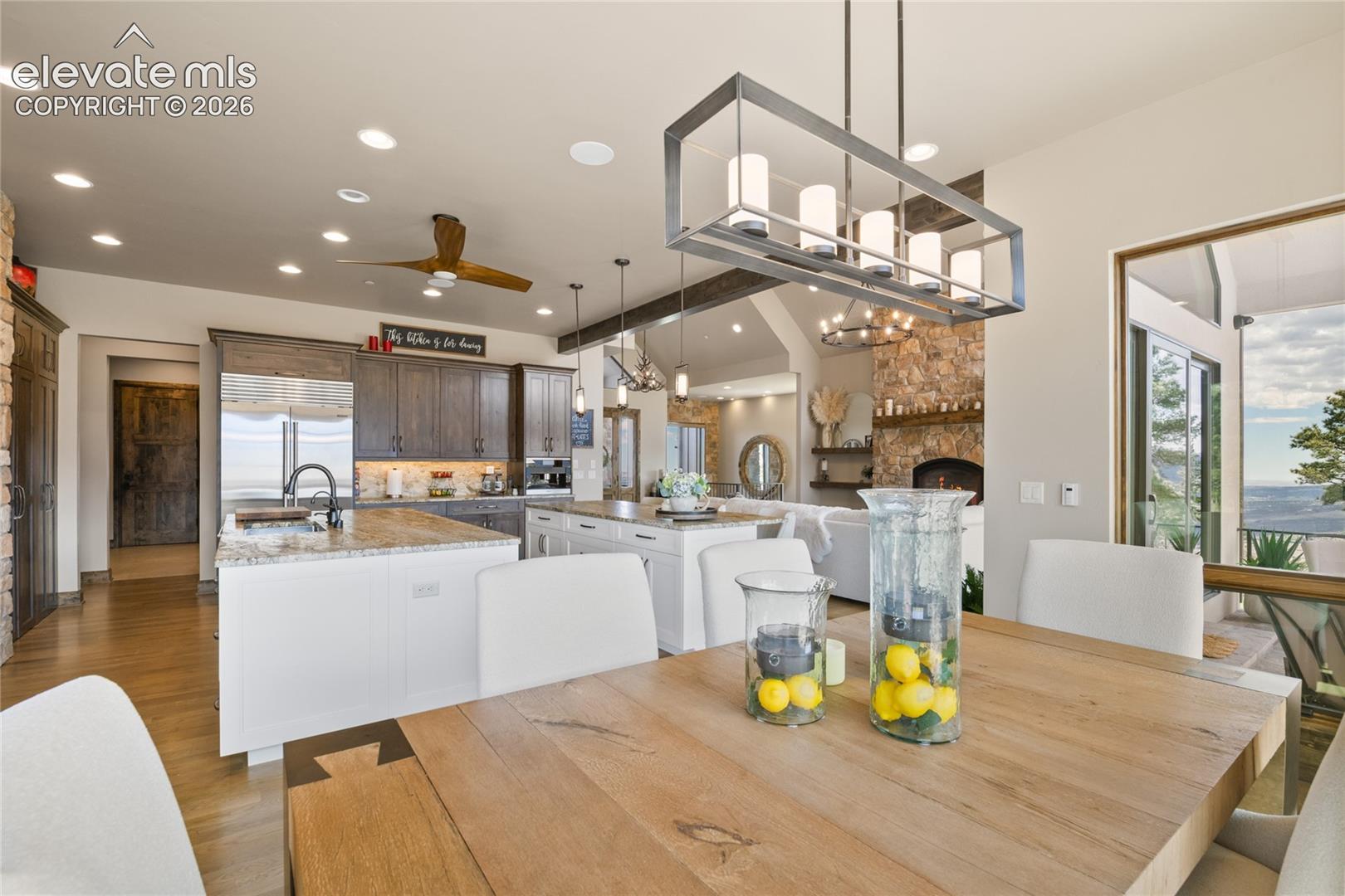 Open-concept great room layout flowing from chef's kitchen to family dining and living, featuring designer lighting, white oak floors, and panoramic views.