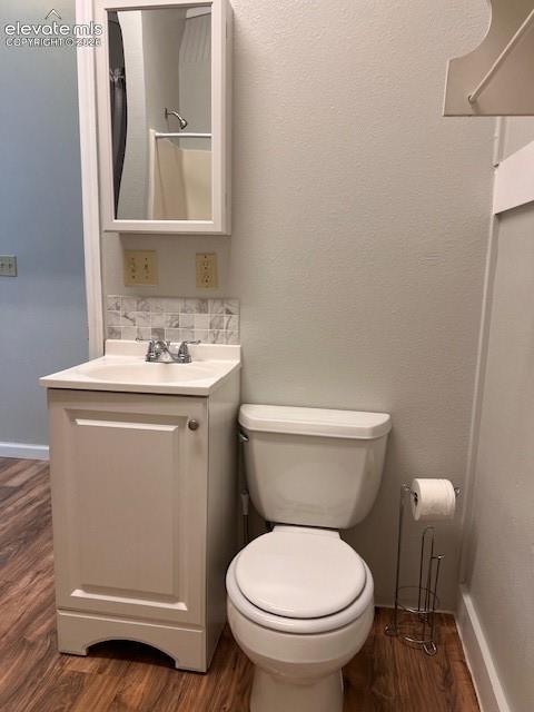 Bathroom featuring wood-finish flooring, a white cabinet vanity with a square sink, stone-finish tile backsplash, and a wall-mounted mirrored medicine cabinet