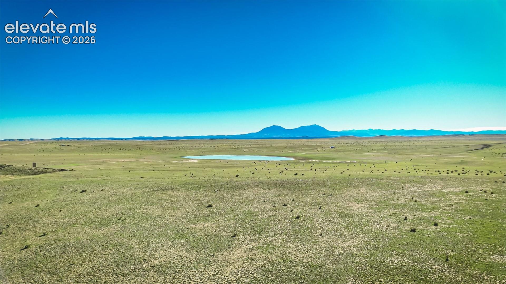 Expansive acreage featuring natural grasslands, a central pond, and distant mountain backdrops
