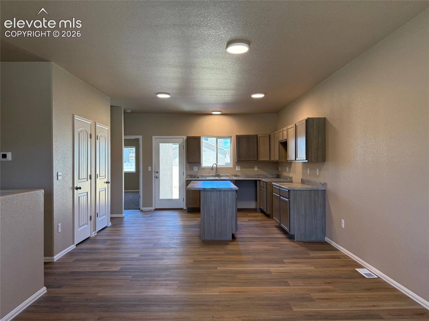Wood-finish flooring throughout, kitchen with an island, stainless steel sink, and light gray countertops, and multiple recessed ceiling lights