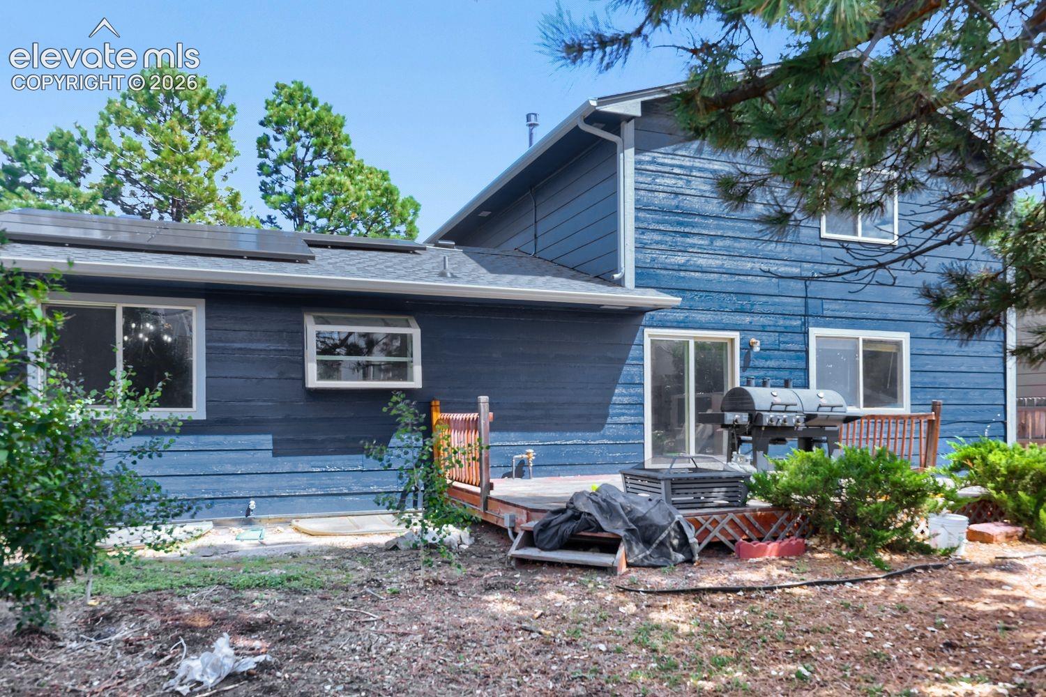 Rear exterior featuring wood siding, multiple windows, a sliding glass door, a wooden deck, and roof-mounted solar panels