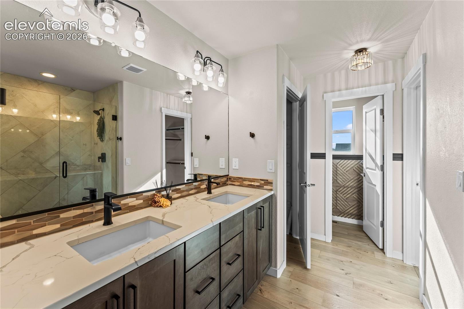 Double vanity with quartz countertop, rectangular undermount sinks, matte black fixtures, full-width mirror, and walk-in shower with glass enclosure