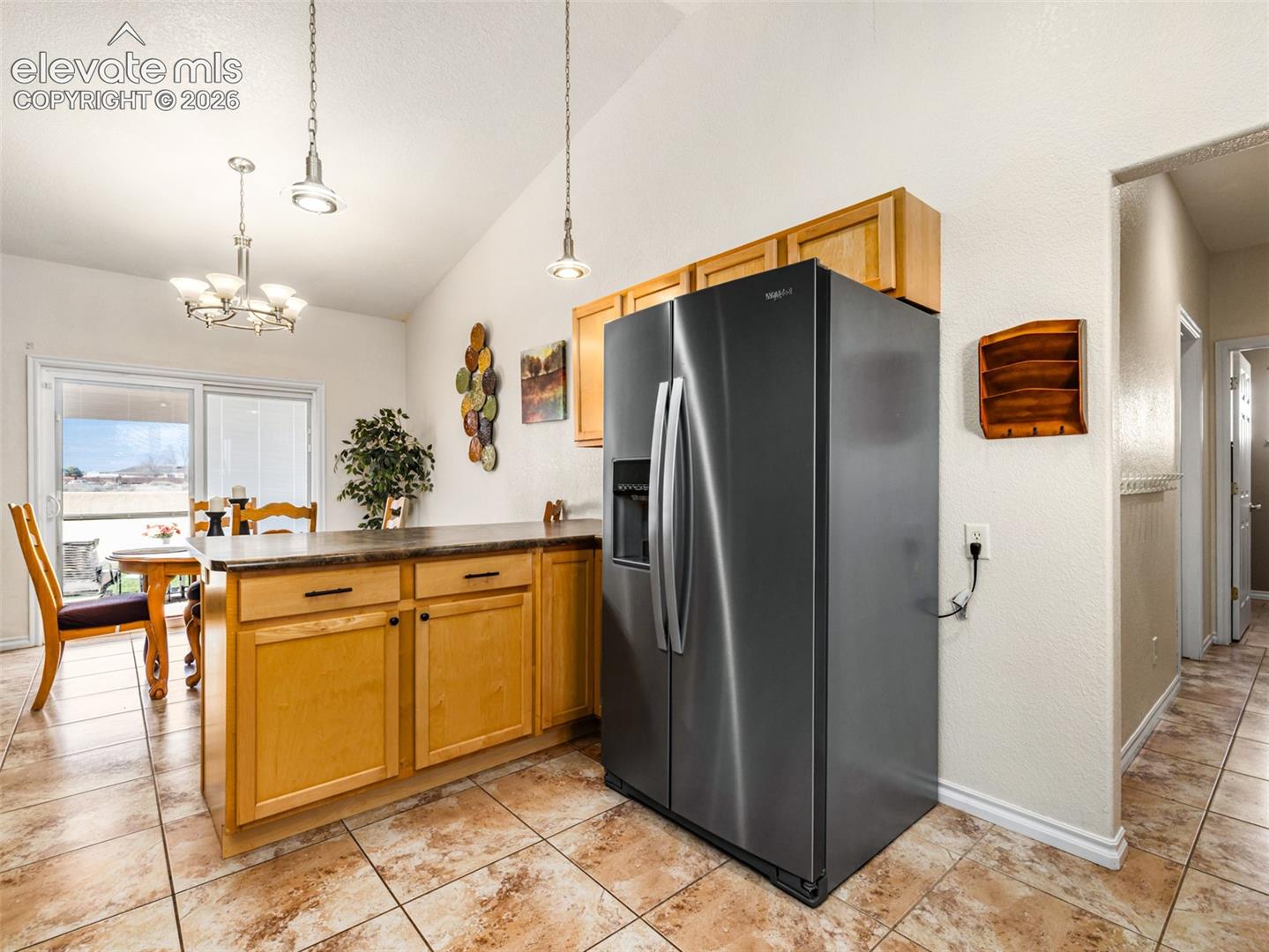 Vaulted ceiling, recessed lighting, wood cabinetry, stainless steel refrigerator, and tiled flooring