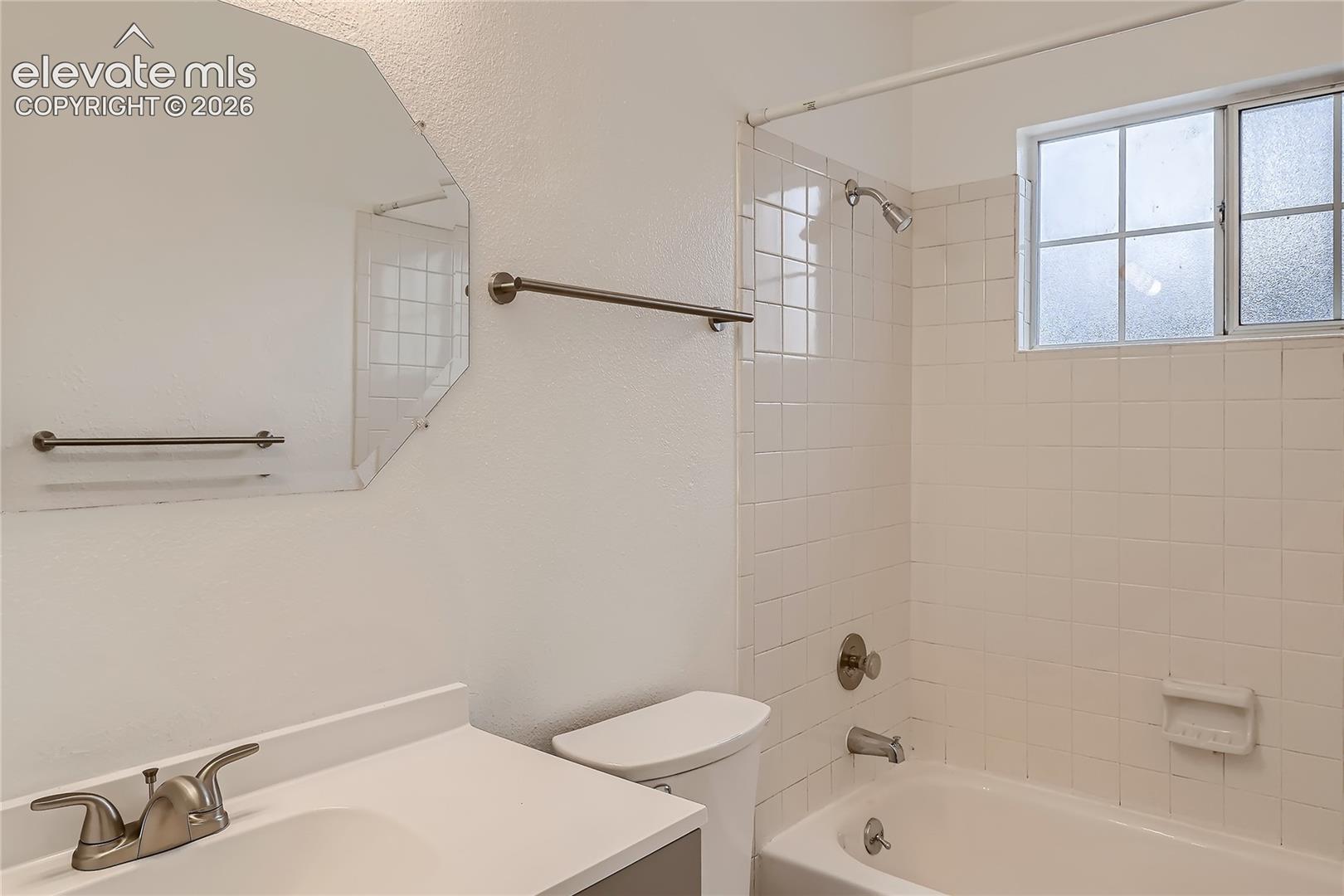 Bathroom featuring a vanity with integrated sink, octagonal mirror, porcelain tile shower surround, and a metal-finish faucet
