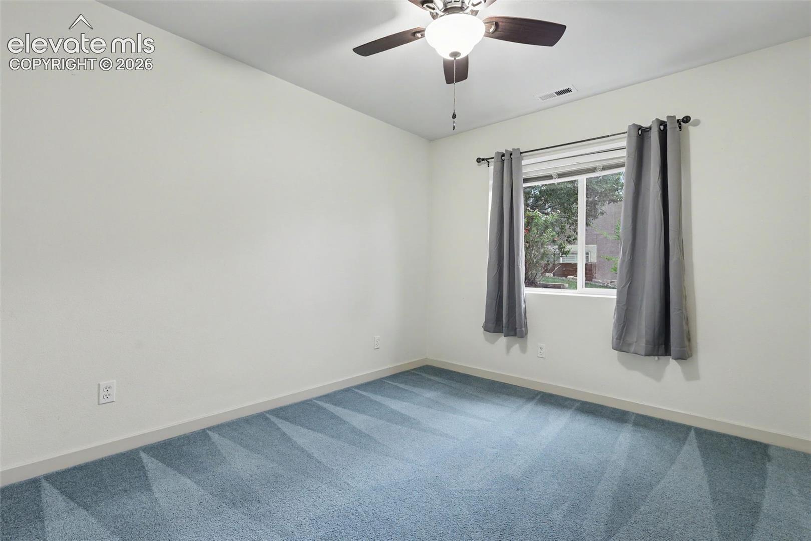 Room featuring light blue patterned carpeting, a ceiling fan with integrated lighting, and a window with dark gray curtains