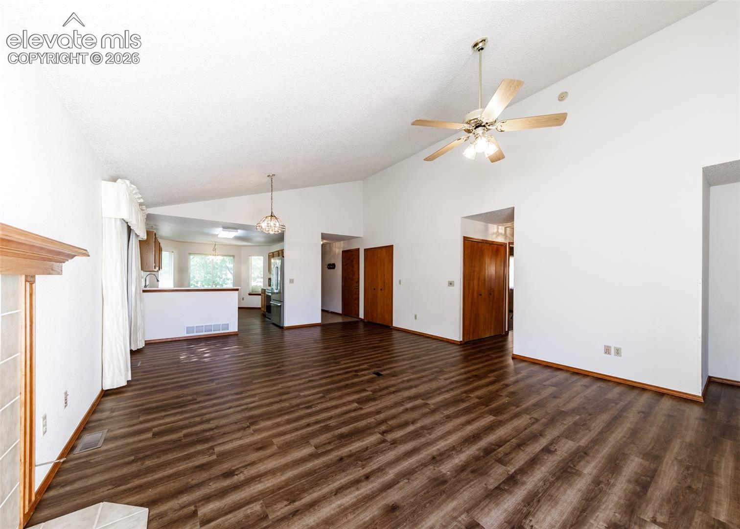 Vaulted ceiling, wood-finish flooring, ceiling fan, fireplace with wood mantel, and a kitchen with wood cabinetry