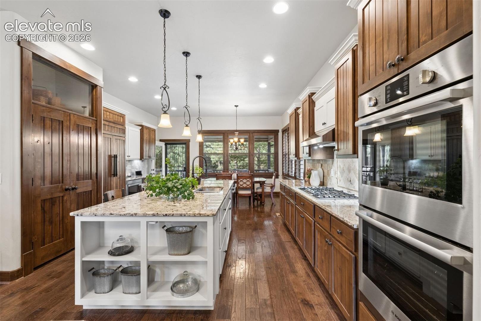 Kitchen featuring a center island with open shelving and stone countertop, stainless steel double wall ovens, recessed lighting, wood-finish flooring, and natural wood cabinetry
