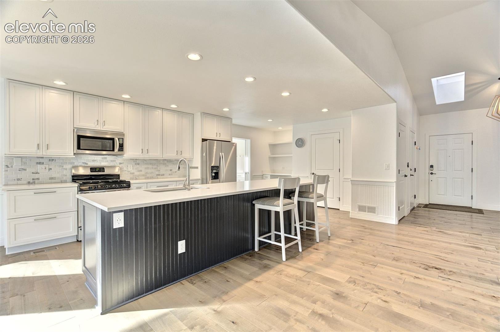 Kitchen featuring white cabinetry, an oversized island with beadboard detailing, quartz countertops, stainless steel appliances, and wood-finish flooring