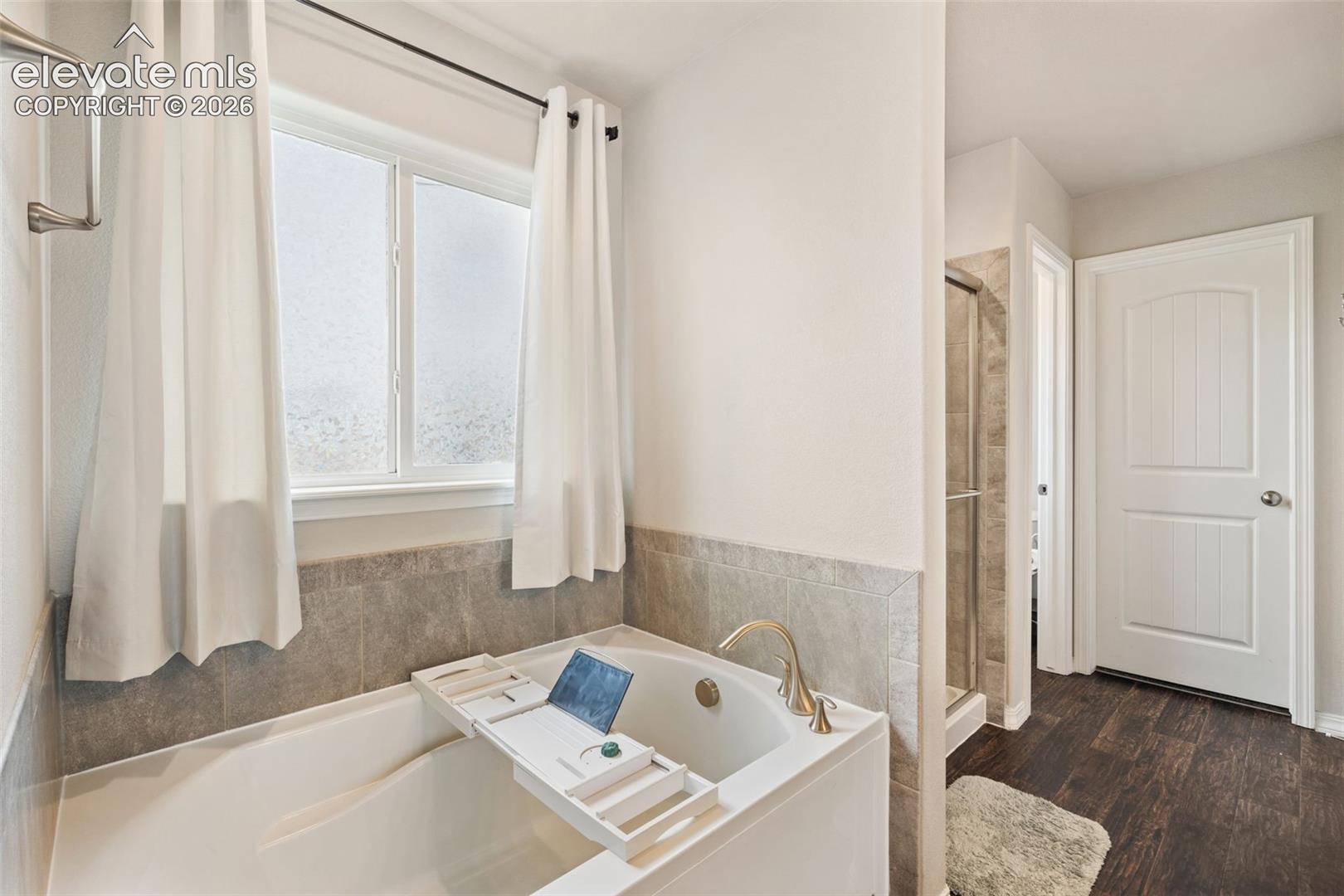 Soaking tub with brass-finish fixtures, a tiled surround, and a privacy window