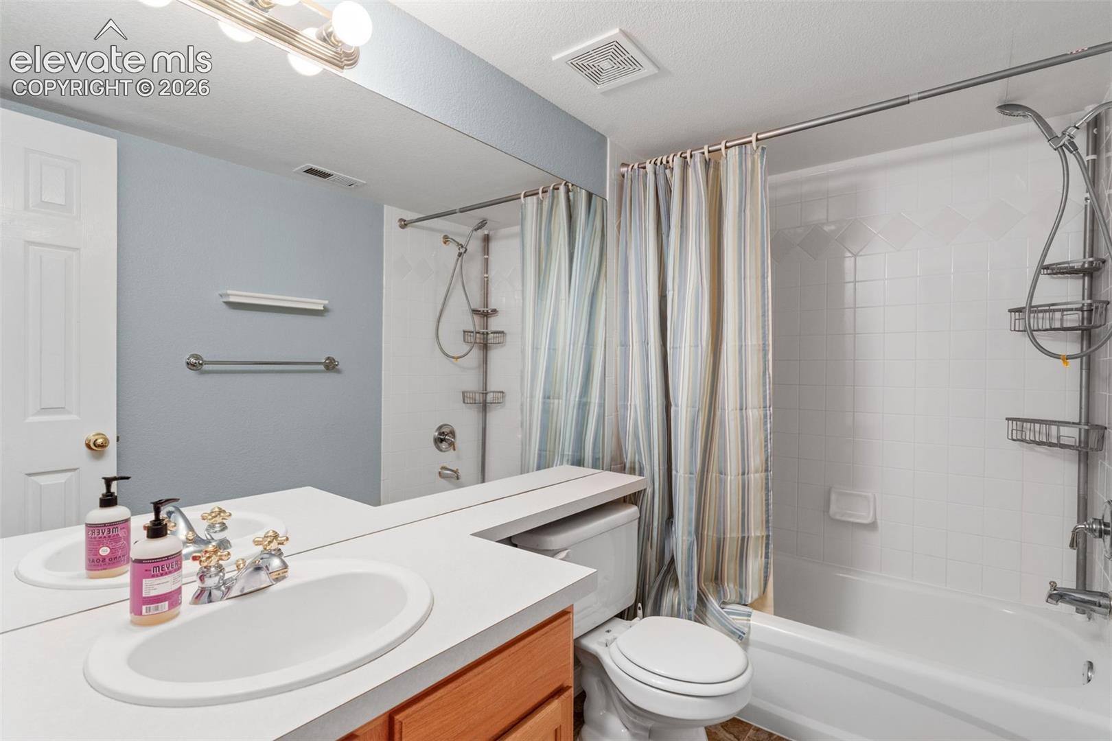 Bathroom featuring a vanity with an integrated countertop, oval sink, chrome-finished hardware, full-width wall mirror, and a tub-shower combination with white tiled walls