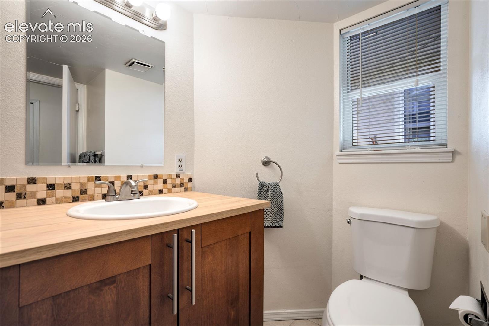 Wood-finish vanity with a light-toned countertop, undermount sink, multi-colored square tile backsplash, and oversized mirror