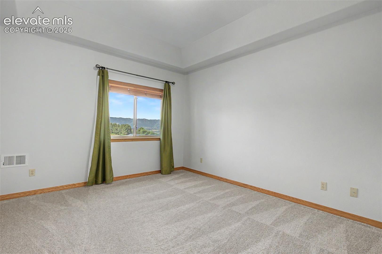 Carpeted room featuring a large window with wood trim, offering a backdrop of distant hills and trees