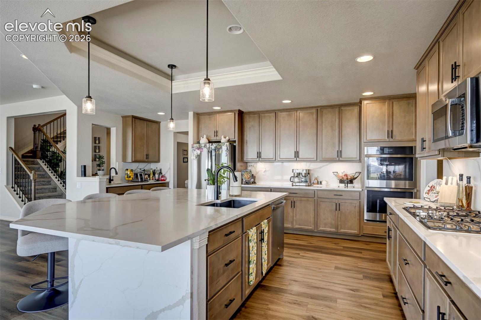 Gourmet kitchen featuring a large island with a waterfall countertop, wood-finish flooring, stainless steel appliances, built-in double ovens, and recessed lighting