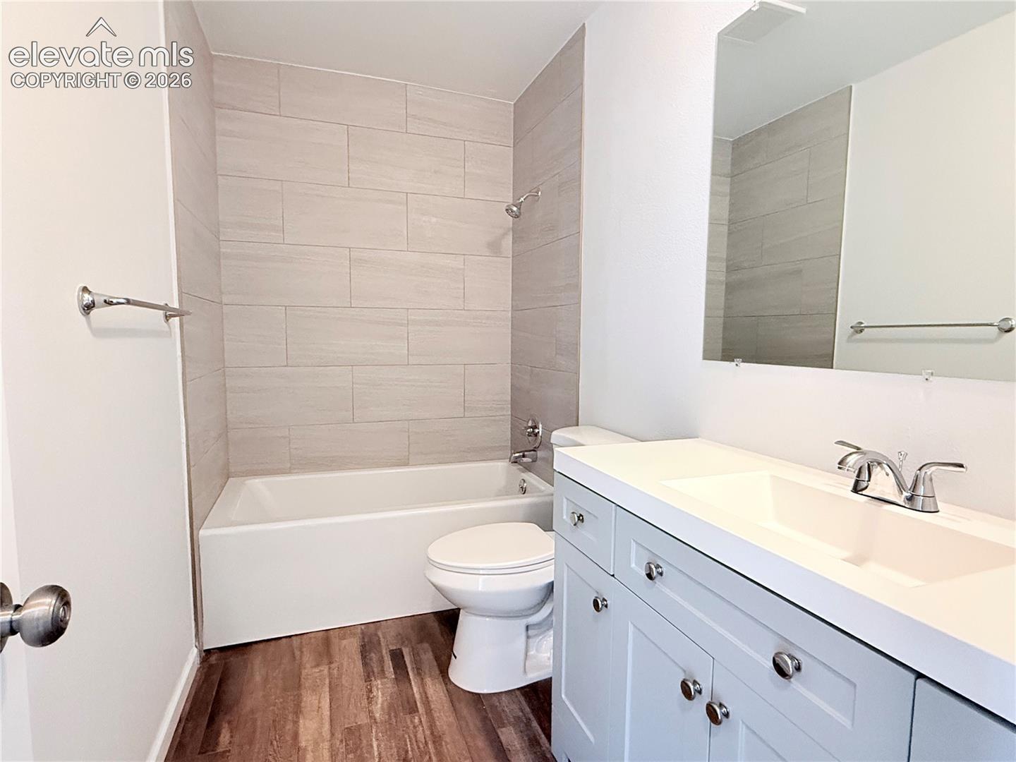 Bathroom featuring a white bathtub, tiled shower surround, wood-finish flooring, and a vanity with an integrated sink
