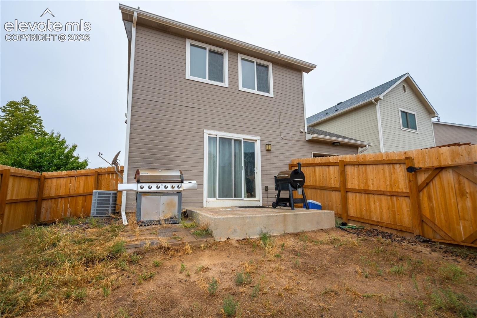 Rear exterior with siding, two upper-level windows, a ground-level sliding glass door, a concrete patio, and a wood fence enclosure