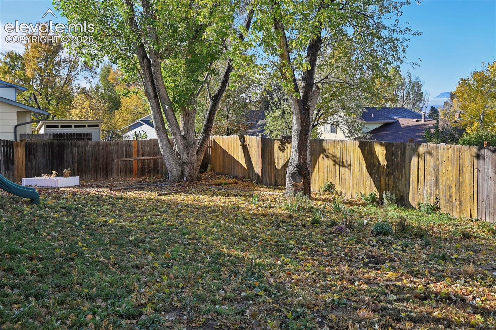 Great Backyard featuring vertical wood-plank fencing, mature deciduous trees, and a grass lawn