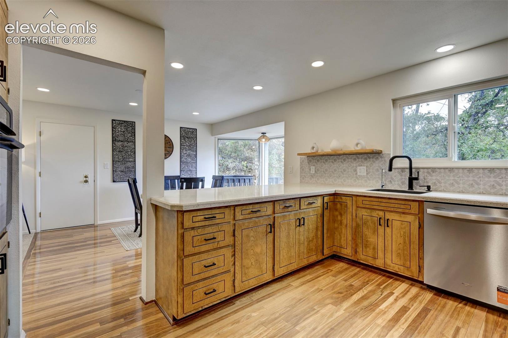 Kitchen featuring light wood-finish cabinetry, stone-style countertops, matte black faucet, stainless steel dishwasher, and recessed lighting