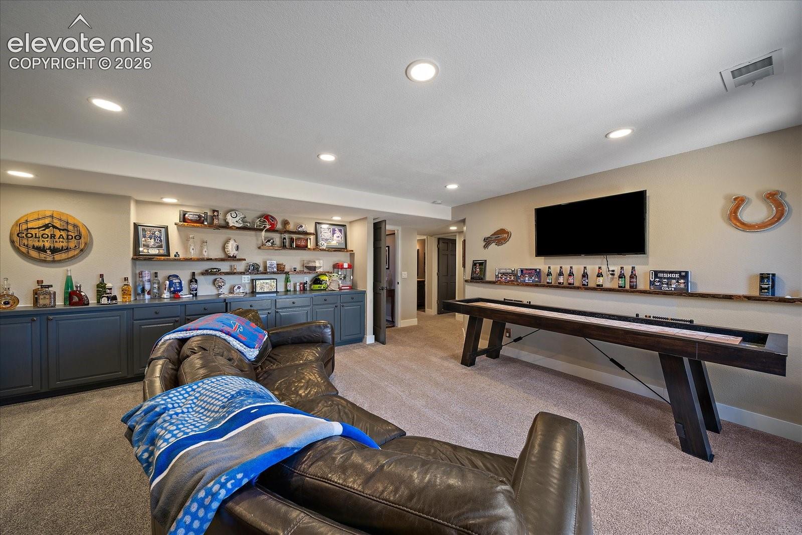 Finished interior room with recessed lighting, wall-to-wall carpeting, built-in lower cabinetry with matte finish, and custom live-edge wood floating shelving