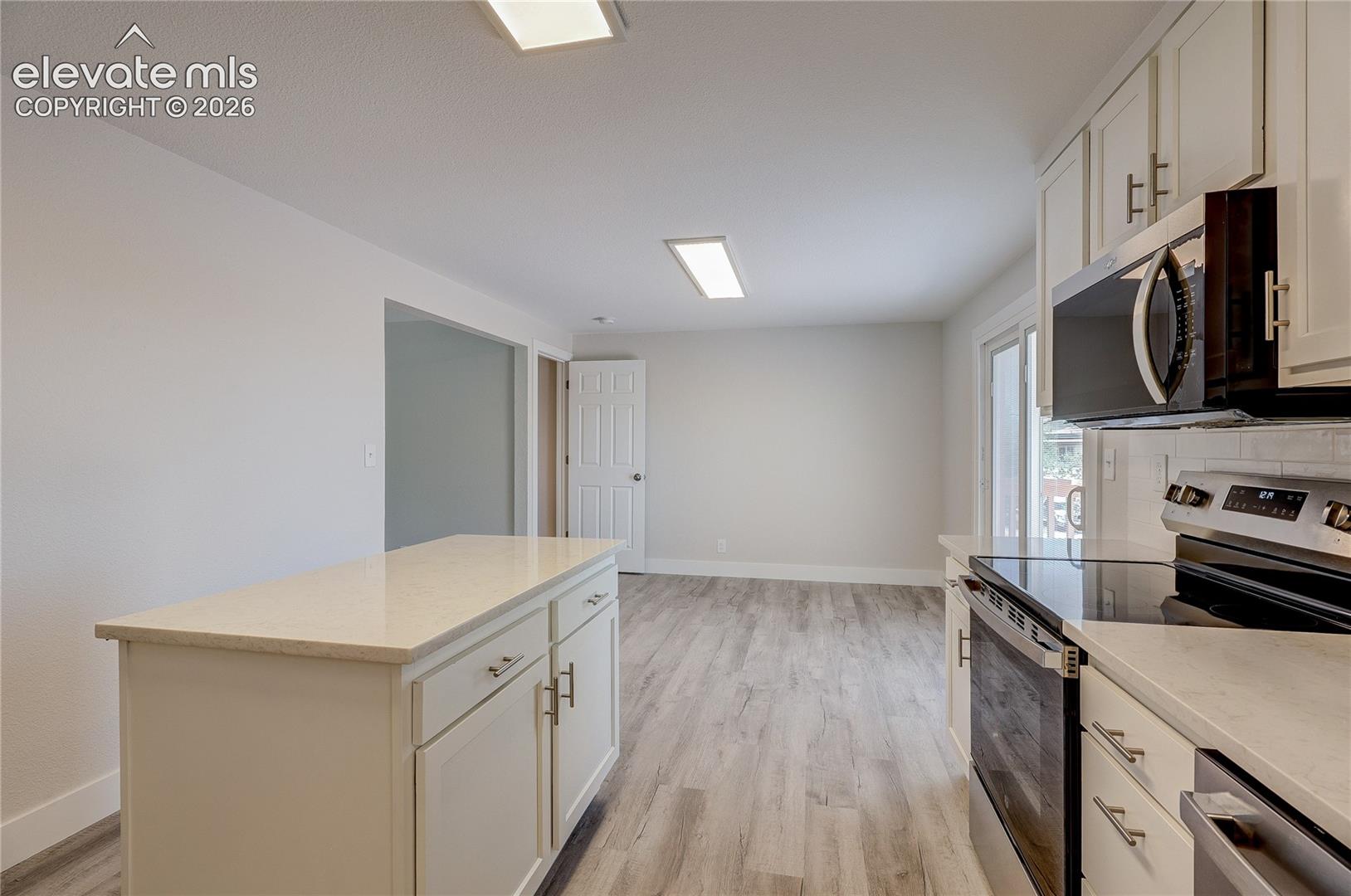 Kitchen featuring a center island, light-toned composite countertops, white cabinetry with brushed-metal pulls, stainless steel appliances, and wood-finish flooring