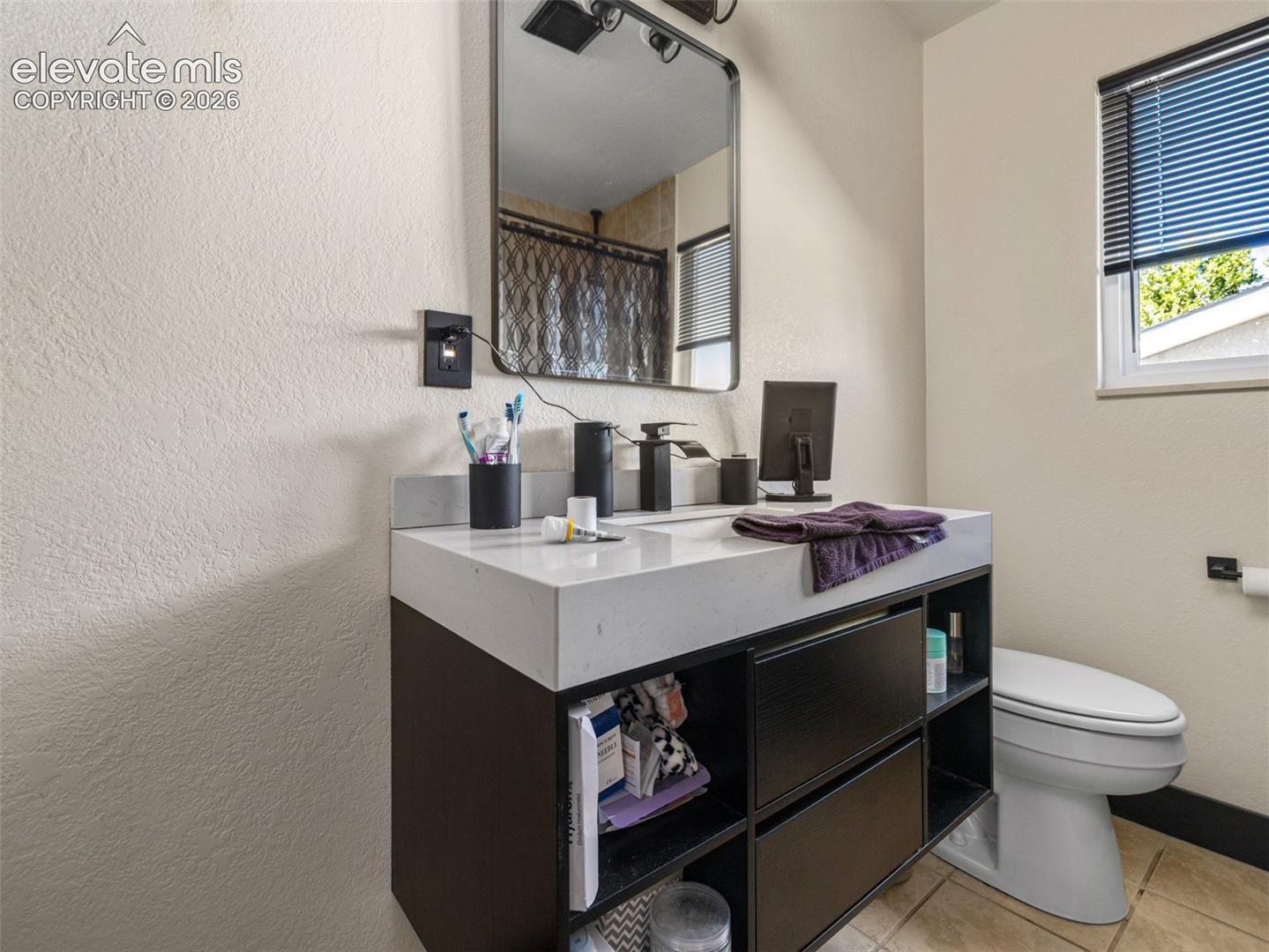 Modern vanity with a white countertop and dark wood-finish cabinetry, rectangular mirror, and a window with blinds
