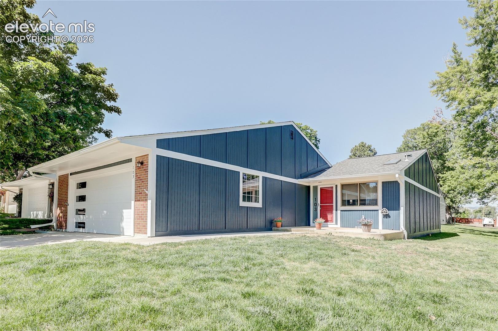 Single-story exterior featuring vertical board-and-batten siding, brick accents, an attached two-car garage with glass-paneled door, and a concrete entry pad