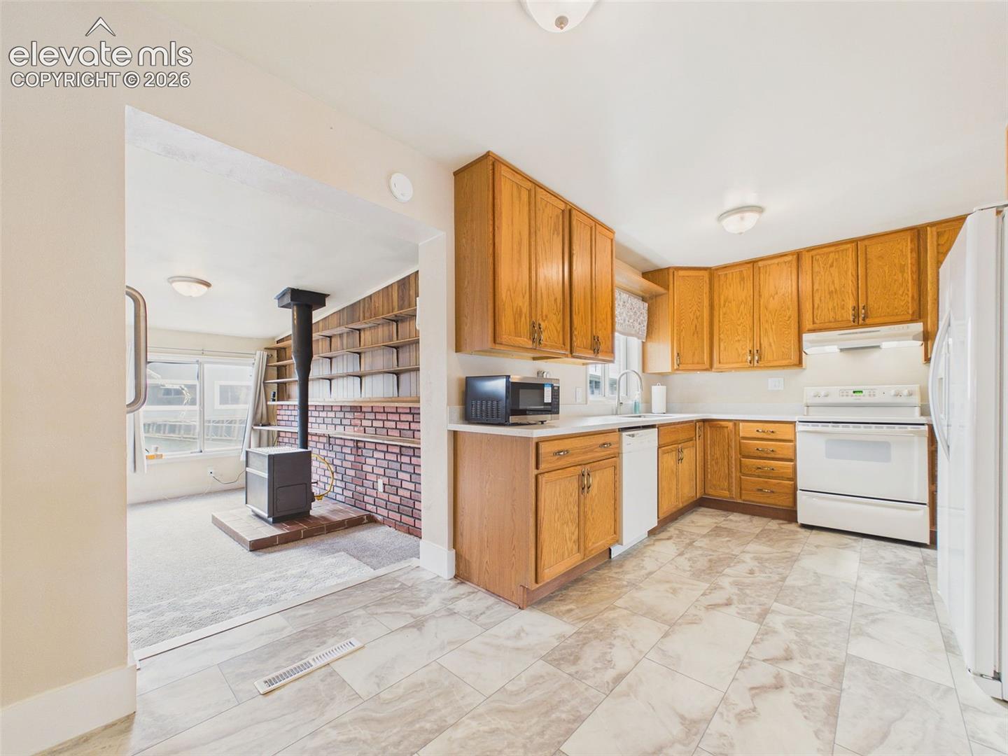 Bright kitchen with extensive cabinet storage, white appliances, attractive tile-look flooring, and a window above the sink.