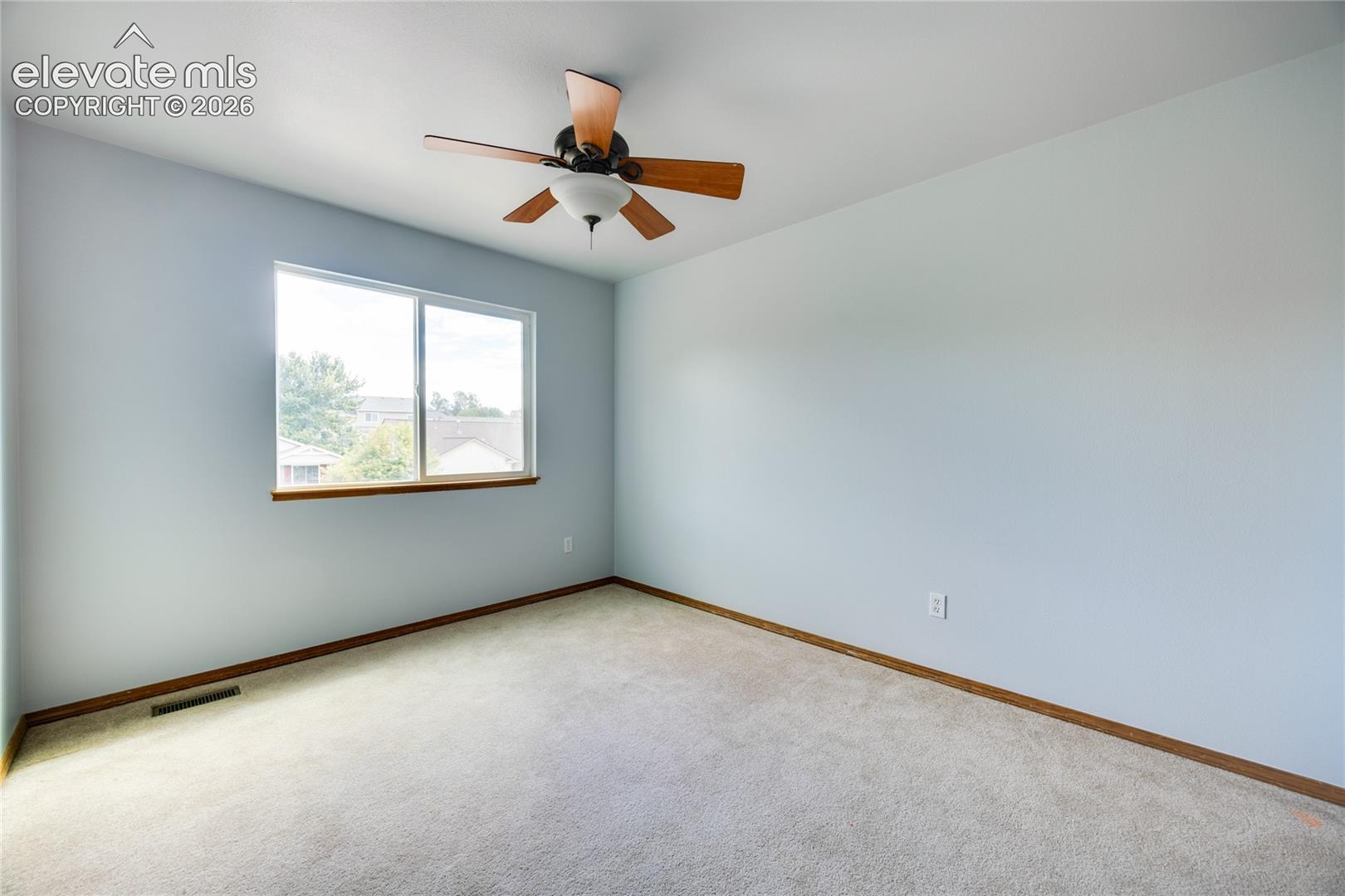 Light gray wall paint, light-colored carpet flooring, a window with wood-finish trim, and a ceiling fan with integrated lighting