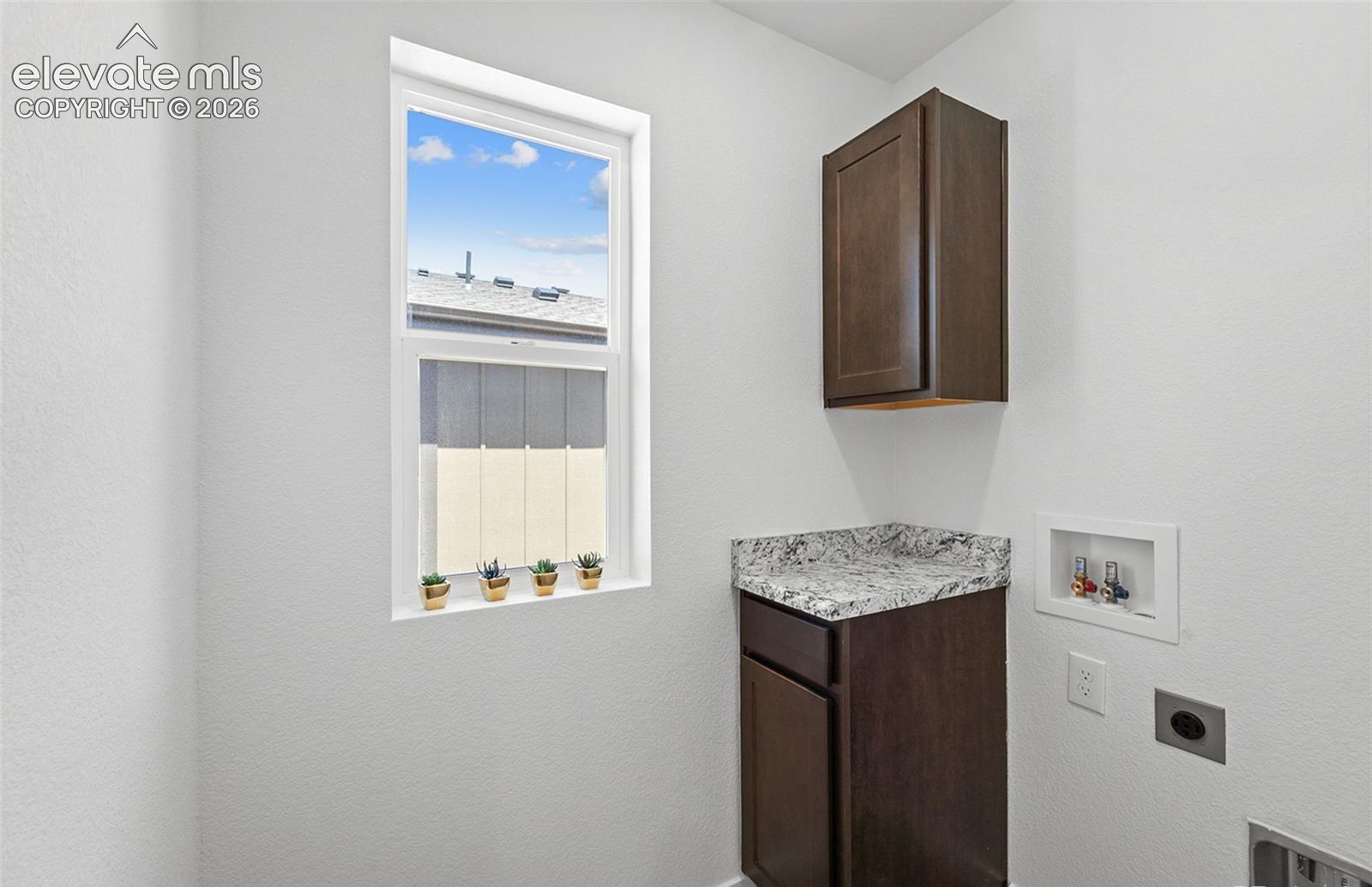 Utility space featuring dark-finish cabinetry, a stone-patterned countertop, a recessed utility box, and a single-hung window