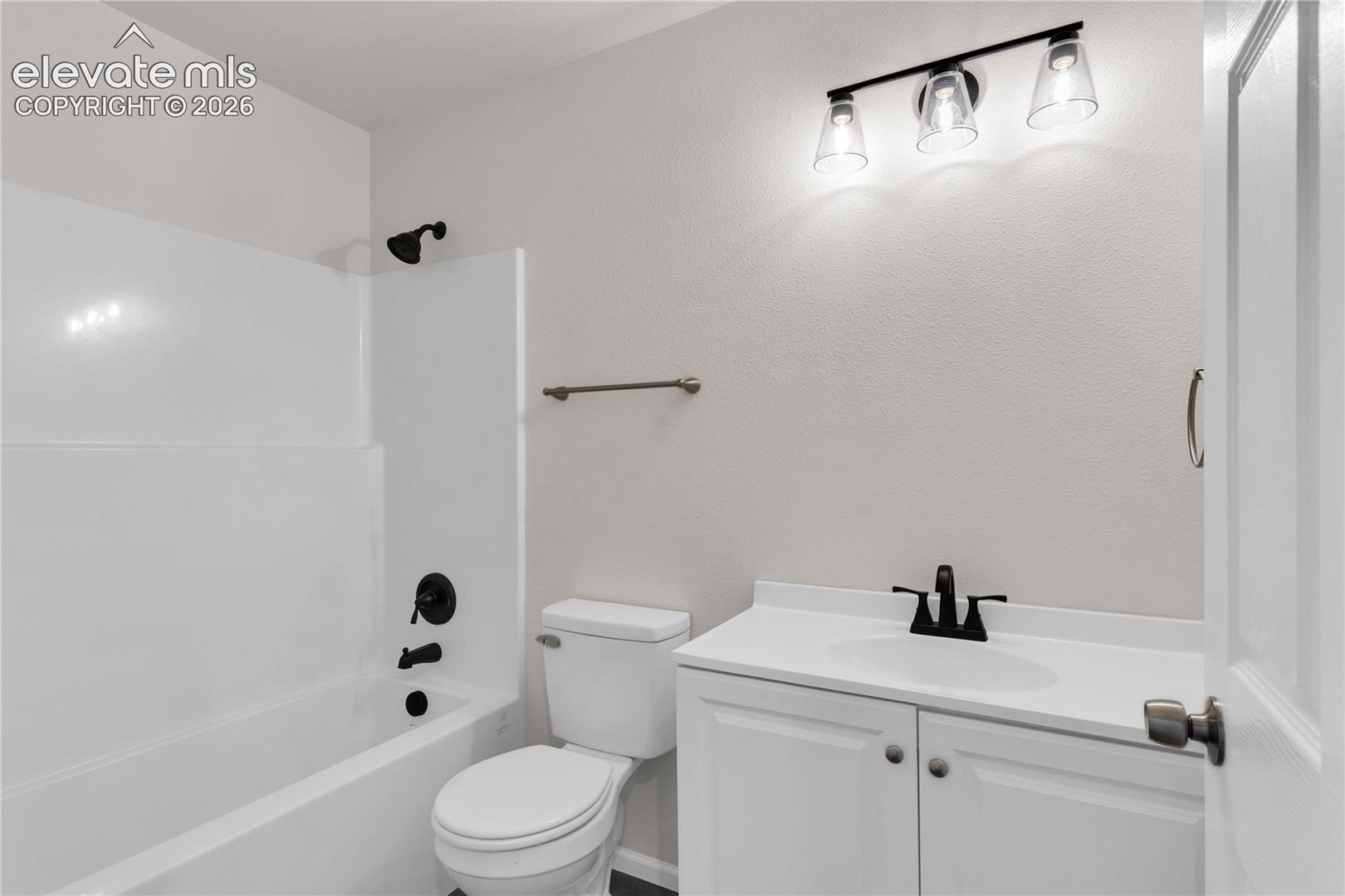 Bathroom featuring a vanity with a white countertop and integrated sink, matte black faucet and shower fixtures, tub-and-shower combination with white wall surround, and a three-light wall-mounted fixture