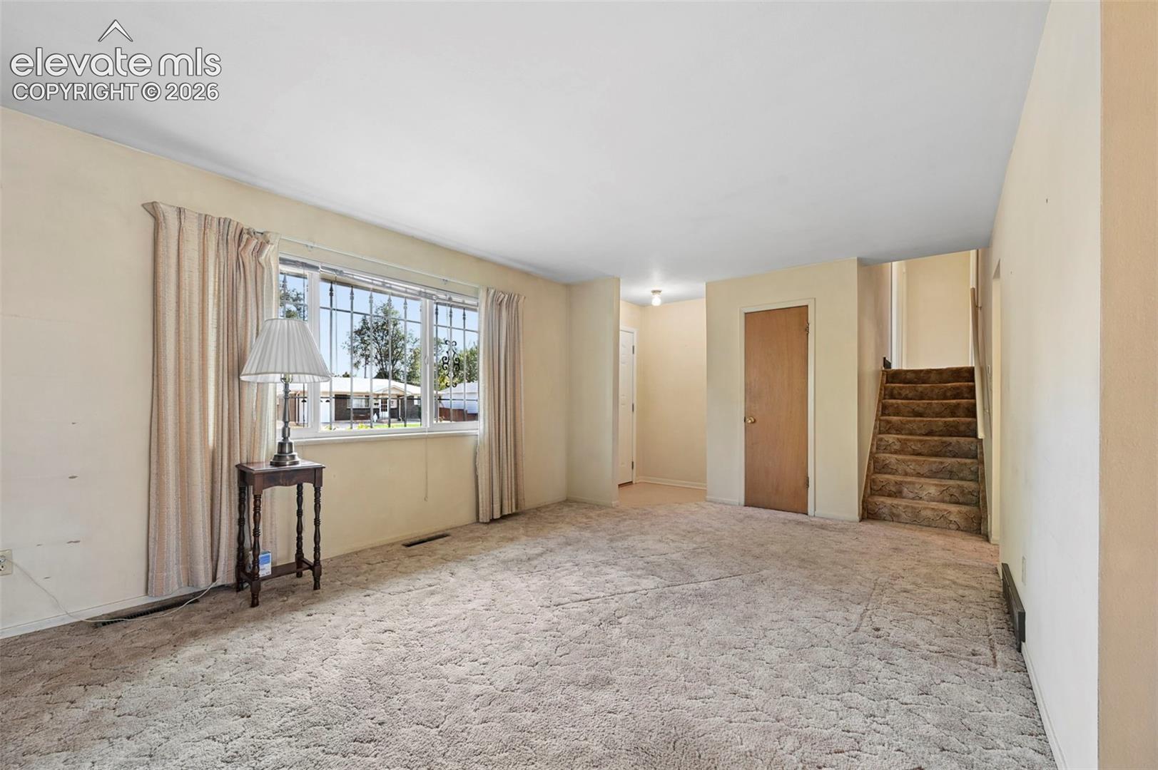 Living area featuring large window, textured wall-to-wall carpeting, and a staircase with carpeted treads
