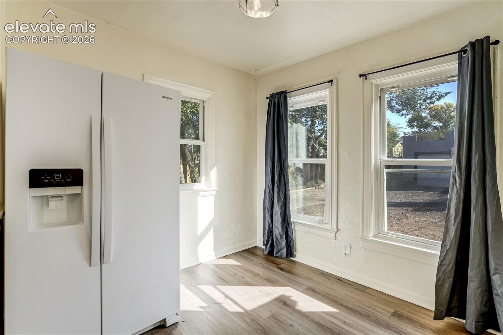 Wood-finish flooring, white side-by-side refrigerator, and multiple windows with mullion detailing